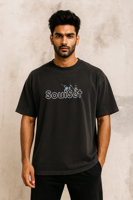 Black oversized t-shirt featuring a large white spider graphic intertwined with delicate blue cherry blossom branches printed on the back, worn by a male model facing away from the camera.