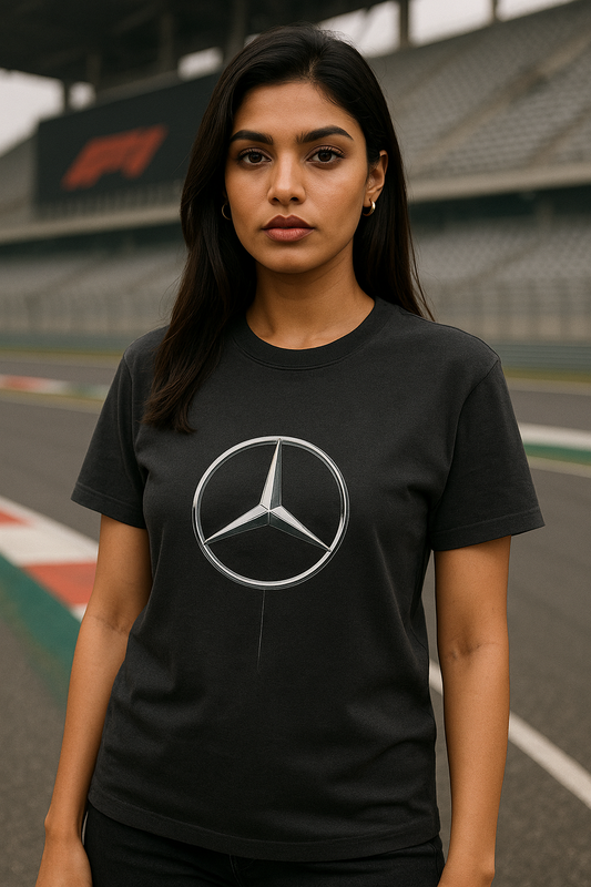 A confident Indian female model with fair skin and a fit physique stands in a relaxed pose, facing away to showcase the FRONT of her black oversized Mercedes-AMG Petronas F1 Team t-shirt. The t-shirt features bold white   “MERCEDES-LOGO,” “PETRONAS F1 TEAM,”   The model is positioned on a Formula 1 pit lane at sunset, with a sleek Mercedes-Benz garage in the background, exuding a bold and stylish F1-themed atmosphere.